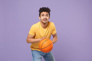 Young african american guy basketball player in casual yellow t-shirt posing isolated on pastel...