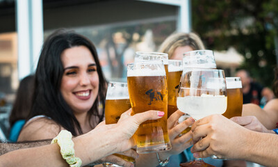 Group of happy friends celebrating and toasting with beer at a bar in summer