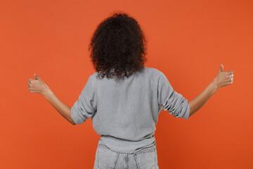 Back rear view of young african american woman girl in gray casual clothes isolated on orange wall background studio portrait. People emotions lifestyle concept. Mock up copy space. Showing thumbs up.