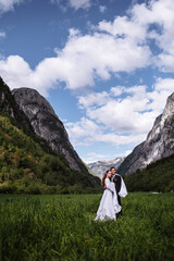 Embracing newlyweds standing in the green juicy grass against the background of mountains