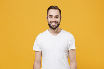 Smiling handsome young bearded man guy in white casual t-shirt posing isolated on yellow wall background studio portrait. People sincere emotions lifestyle concept. Mock up copy space. Looking camera.