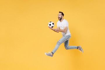 Fototapeta na wymiar Excited bearded man guy football fan in white t-shirt isolated on yellow background. People sport family leisure concept. Cheer up support favorite team with soccer ball, jumping, point finger aside.