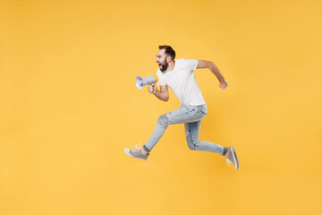 Fototapeta na wymiar Crazy young bearded man guy in white casual t-shirt posing isolated on yellow wall background studio portrait. People lifestyle concept. Mock up copy space. Jumping like running, scream in megaphone.