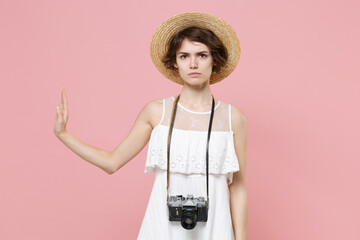 Serious young tourist woman in summer dress hat with photo camera isolated on pink background....