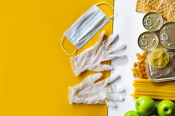 Food delivery, Donation. Food supplies crisis food stock for quarantine isolation period on white and yellow background. Pasta, canned food, apples, oil, crackers, medical mask and gloves.