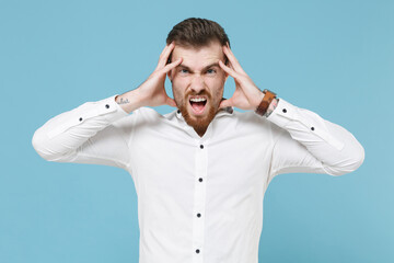 Naklejka premium Displeased tired young bearded man guy 20s in white classic shirt isolated on pastel blue background studio portrait. People sincere emotions lifestyle concept. Mock up copy space. Put hands on head.