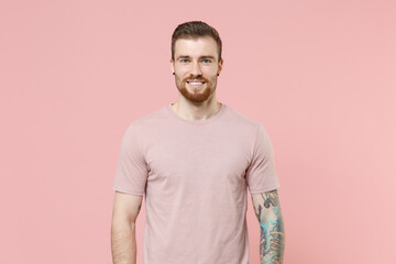 Smiling young bearded tattooed man guy in pastel casual t-shirt posing isolated on pink wall...