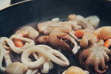 Seafood cocktail in black frying pan. Baby octopus, squid, shrimps, scallop.