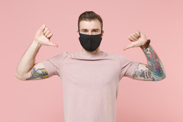 Young tattooed man guy in pastel casual t-shirt, black face mask posing isolated on pink background...