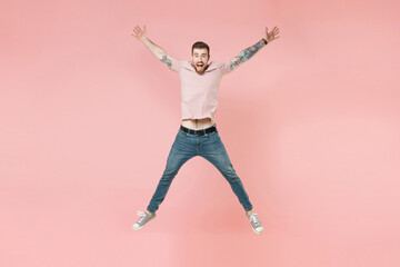 Fototapeta na wymiar Excited young tattooed man guy in pastel casual t-shirt posing isolated on pink background studio portrait. People emotions lifestyle concept. Mock up copy space. Jumping spreading hands and legs.