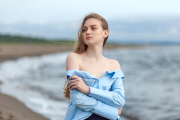 Fototapeta na wymiar Beautiful young blonde girl in a blue shirt relaxing on the sea