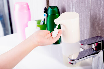 Hands collect liquid soap in a proximity sensor, near the sink with a tap in the bathroom