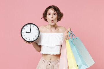 Shocked amazed young woman girl in summer clothes isolated on pastel pink wall background studio portrait. Shopping discount sale concept. Mock up copy space. Hold package bag with purchases, clock.