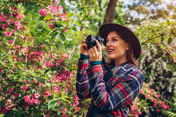 Woman photographer taking pictures using camera in summer garden shooting trees in blossom. Walking...