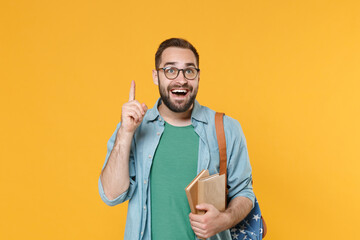 Amazed man student in casual clothes glasses with backpack hold books isolated on yellow background. Education in high school university college concept. Mock up copy space. Pointing index finger up.