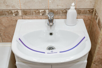 Fototapeta premium Modern bathroom with tiled walls, white sink with disinfectant. Sanitary treatment was carried out against spread of infections.