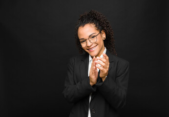 young black woman feeling happy and successful, smiling and clapping hands, saying congratulations with an applause against black wall