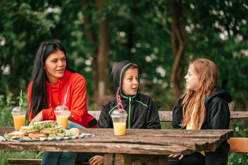 Beautiful mother with two kids eating sandwiches at a picnic table in the forest
