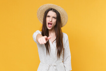 Angry young brunette woman girl in white dress hat posing isolated on yellow background studio portrait. People lifestyle concept. Mock up copy space. Point index finger on camera, screaming swearing.