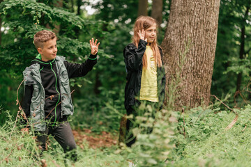 Fototapeta na wymiar Cute kids waving their arms to someone during forest hike