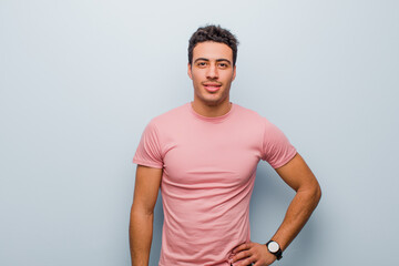 young arabian man smiling happily with a hand on hip and confident, positive, proud and friendly...