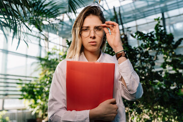 Fototapeta premium Young agricultural engineer working in greenhouse. Young female scientist looking at the camera