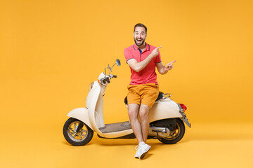 Fototapeta na wymiar Surprised young bearded man guy in casual summer clothes standing near moped isolated on yellow background. Driving motorbike transportation concept. Mock up copy space. Pointing index fingers aside.