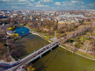 Fototapeta premium Top view on Secheni baths, Budapest city park. People are resting on the green grass. Lakes and bridge in the park. Spring. Trees without leaves and with green leaves.