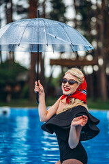 Pin up styled blonde in sunglasses holding umbrella and have fun in the swimming pool