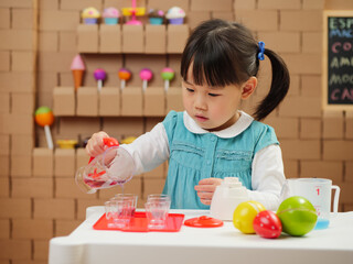 toddler girl pretend play food preparing role against cardboard shop background