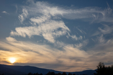 Beautiful white clouds on a background of blue sky. Landscape in the mountains. Sunset sky. Orange sunset.