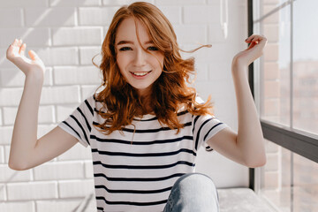 Fototapeta na wymiar Beautiful caucasian girl wears striped t-shirt. Indoor portrait of blissful ginger woman with curly hairstyle.