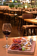 Tabla de quesos y carnes frías acompañada con copa de vino tinto sobre mesa de madera en restaurante
