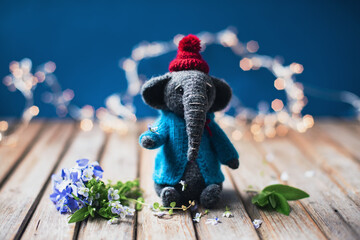 Handmade. Amigurumi toy elephant wearing in the knitted small blue sweater and red hat on the wooden background. Woman's hobby