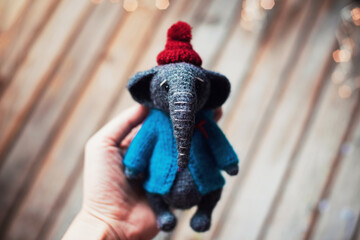 Handmade. Amigurumi toy elephant wearing in the knitted small blue sweater and red hat on the wooden background. Woman's hobby