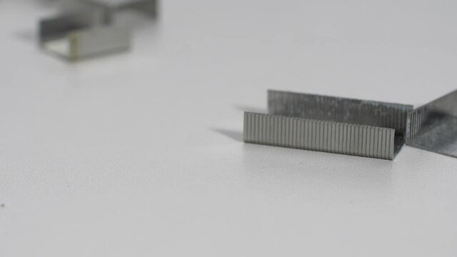 iron shiny clips for a furniture stapler fall onto a white table and crumble bouncing in slow motion. homogeneous background. 180 fps