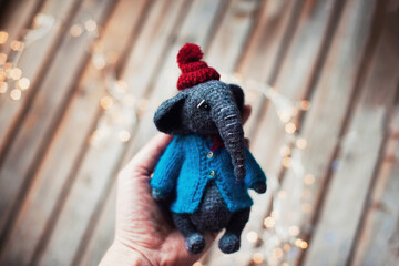Handmade. Amigurumi toy elephant wearing in the knitted small blue sweater and red hat on the wooden background. Woman's hobby
