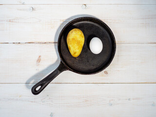 Fried eggs with potato in cast iron pan.