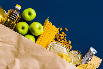 Food delivery, Donation. Food supplies crisis food stock for quarantine isolation period on blue background. Pasta, canned food, apples, oil, crackers.