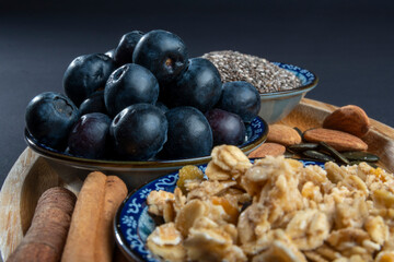 Healthy/natural food concept: On wooden board, some cinnamon sticks, almonds and sunflower seeds. In front and back blurry crunchy granola and chia seeds. Focused on blueberries in center