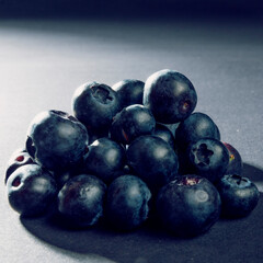 Very close up on natural and organic blueberry fruits stacked to a pyramid shape. Light falls from behind on dark background