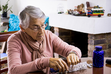 Senior woman at home arranging her prescription drugs into  weekly pill organizer