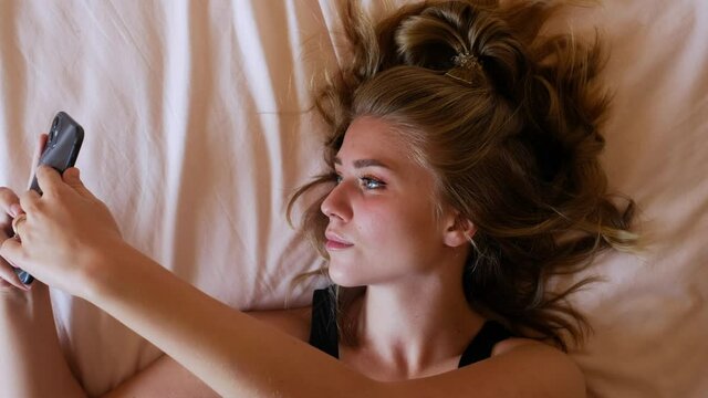Young woman lying on bed and taking selfie