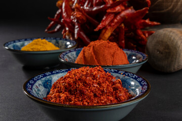 Close up on a blue bowl with granular red pepper. Blurry in background powdered red pepper, yellow...
