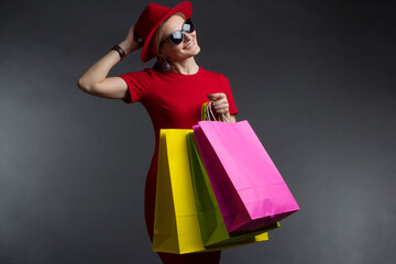 a blonde in a red dress and sunglasses poses on a dark Studio background