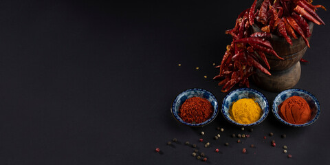 Top view on three blue bowls with whole, granular and powdered red pepper and yellow mixed ginger,...