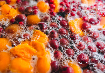 Fototapeta na wymiar Fresh fruits are boiled in boiling water in a metal pan on a stove with bubbles and foam close-up. Cooking a delicious compote of apricot, apples, cherries, raspberries. Photography, concept.