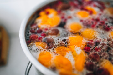 Fresh fruits: apricots, cherries, raspberries, apples are boiled in boiling water in a metal pan on a stove with bubbles and foam close-up. Cooking delicious homemade compote. Photography, concept.