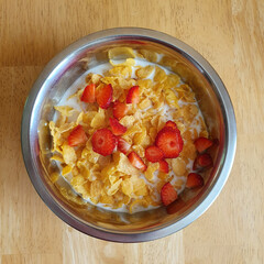 Breakfast food: corn flakes with strawberry peaces and milk in a metal plate