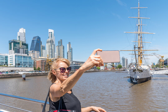Horizontal image of an adult blonde woman taking a selfie with Puerto Madero, Buenos Aires in the background